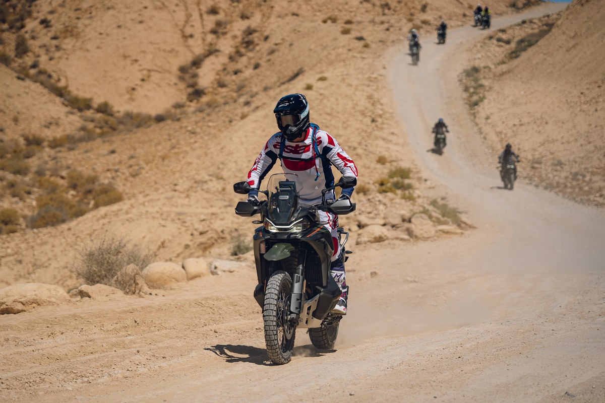רוכב נוסע לעבר המצלמה בשביל עפר בנגב על CFMOTO 1000MT-X בגוון Tactical Green כהה, ומאחוריו שיירת רוכבים על השביל המתפתל במעלה המדרון